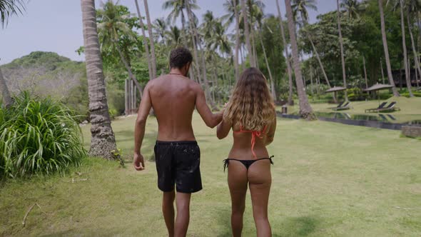 A Backside View of a Young Couple Roaming in a Garden Area with Keeping Hand in Hand