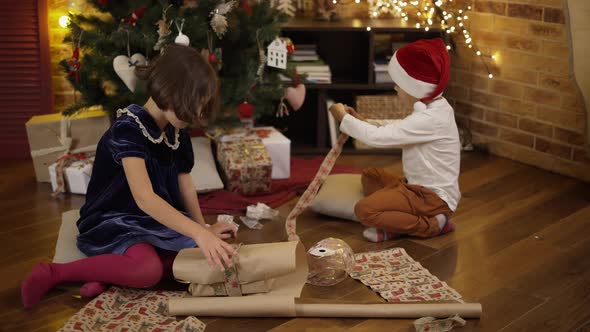 Cute Little Girl and Her Brother Wrapping Christmas Present