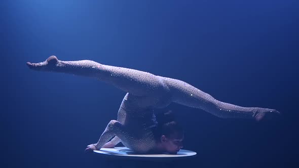 Girl Acrobat on the Table Shows the Tricks of Standing on His Hands. Smoke Background. Slow Motion