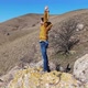 Man Stands on a Stone on a Hillside with His Hands Up and Enjoys Freedom Shooting Drone - VideoHive Item for Sale