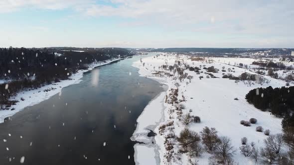 Vast river in winter season during heavy snowstorm, aerial fly forward view