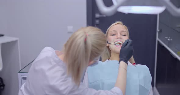 Woman Dentist Examines the Teeth of a Girl Patient in a Dental Chair