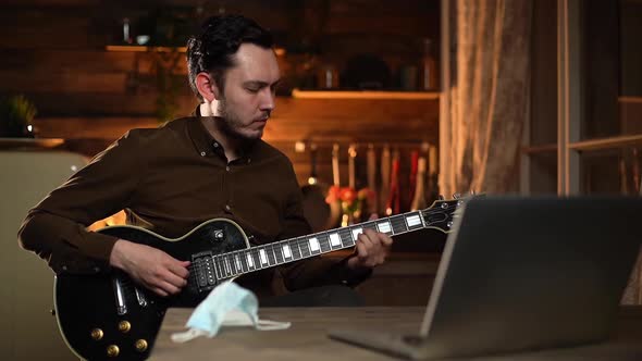 Young Caucasian Man Is Watching Online Tutorial and Learning To Play Guitar.