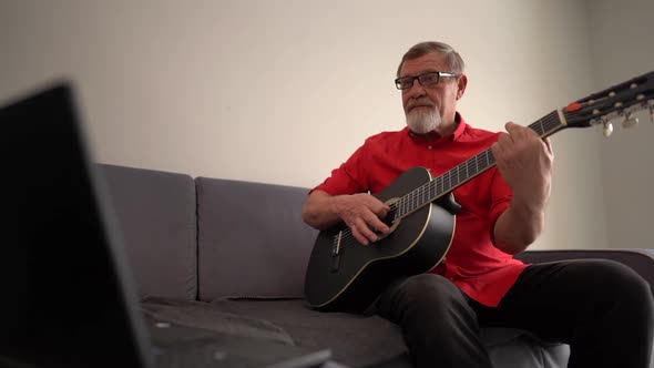 Mature Man Learns To Play the Guitar Online While Sitting on the Couch Near the Laptop