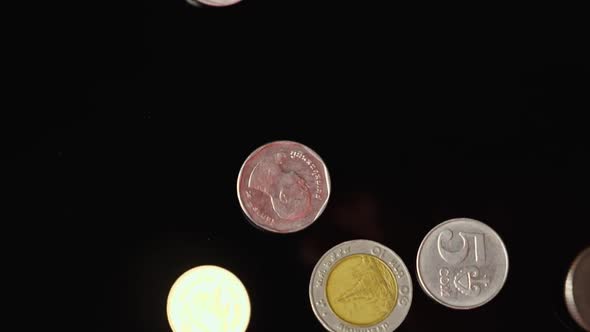 European and Asian coins fall on a black mirror background in slow motion. Close-up