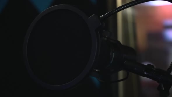 Black studio microphone with a pop filter in recording studio. Panning shot, slow motion, close up