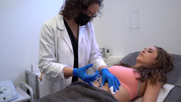 Cosmetologist making injection in belly of woman