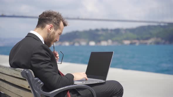 Stressed businessman working on laptop by the sea.