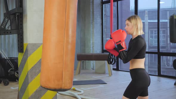 Fit Athletic Woman Kickboxer Punches and Hits the Punching Bag During a Workout in a Loft Gym
