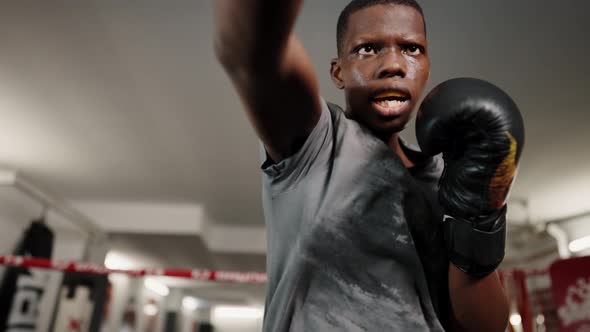 Young Focused African Male Fighter Wearing Black Boxing Gloves Throwing Punches on Ring