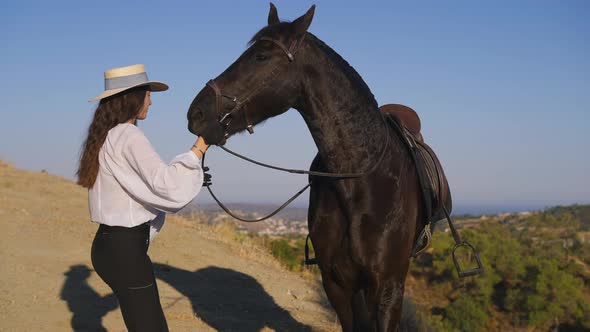 Female Rider Training Horse in Sunny Summer Mountains Holding Bridle Smiling As Gorgeous Graceful