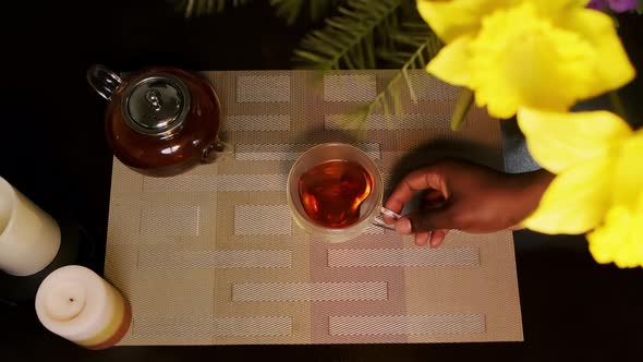 Top down shot of an African American man picking up a transparent heart-shaped glass tea cup from a