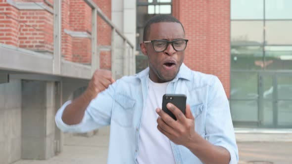 African Man Celebrating Success on Smartphone While Walking in Street