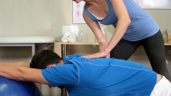 Female physiotherapist assisting man with exercise ball