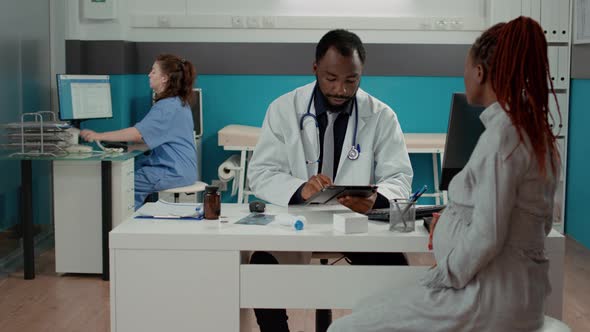 General Practitioner Taking Notes on Digital Tablet at Maternity Checkup