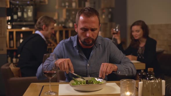 Caucasian Middleaged Male in Jeans Shirt Actively Eating Salad at Restaurant While Pair of Lovers