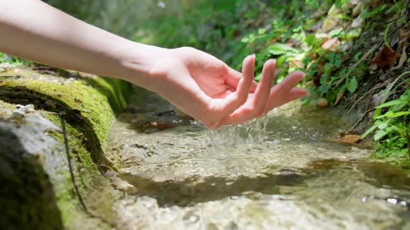 Hand touching flowing stream water.