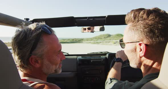 Happy caucasian gay male couple driving car and talking on sunny day at the beach