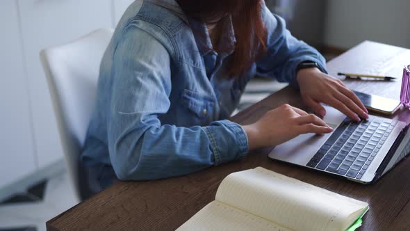 Woman in Denim Shirt Works at Laptop While Sitting at Home in the Kitchen