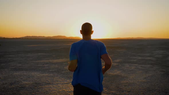 Athletic man working out with battle ropes on a dry lake at sunset