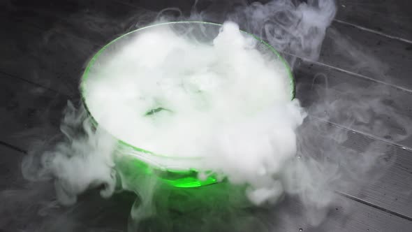 Green Liquid Boils Giving Off Smoke in a Glass Bowl on a Black Background