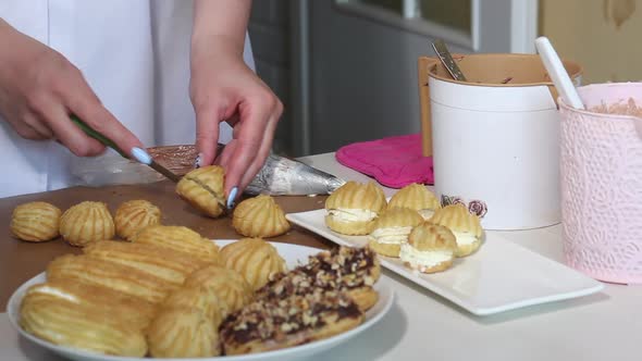 A Woman Cuts Homemade Eclairs. Homemade Eclairs With Cream Lie On A Plate. Pastry Pastries