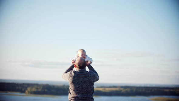 Young Father Playing with His Baby Daughter on the Field - Throwing Her Up