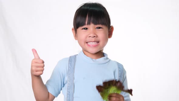 Happy little girl with fresh salad with showing thumbs up on white background in studio