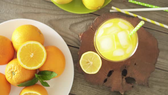 Chilled Lemonade In Glass With Ice Cubes. Tropical Soda On Wooden Table. Plate With Oranges, Mint