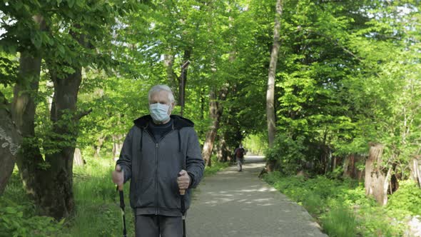 Active Senior Old Man in Mask Training Nordic Walking in Park During Quarantine
