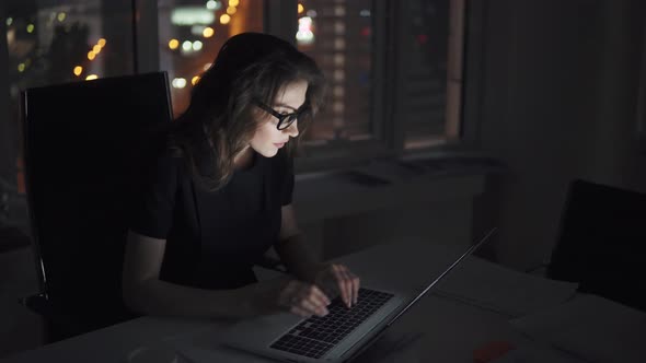 Portrait of a Young Attractive Business Woman Working on a Laptop Late in the Evening in the Office