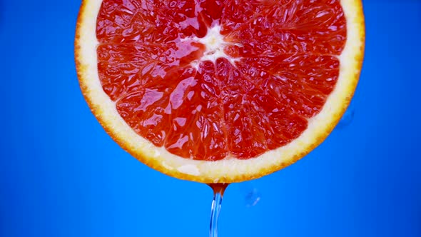 Juicy Grapefruit in Blue Background Closeup Fresh Cool Water is Pouring Over Bright Red Pulp