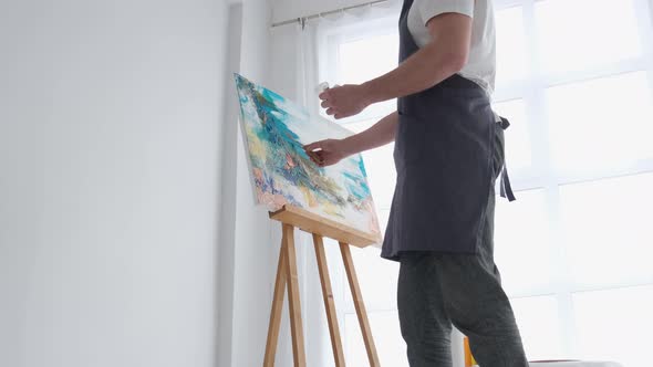 A Young Male Artist Works in a Studio He Uses Bright Paint on a Large White Canvas