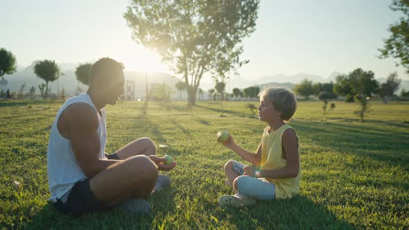 Family Leisure and People Concept  Happy Father Juggling Apples and Son Learning