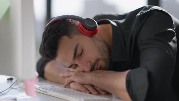 Closeup Portrait of Exhausted Young Middle Eastern Man in Headphones Sleeping on Table at Computer