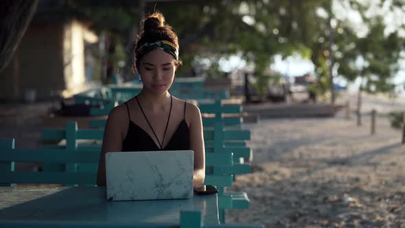 Young influencer girl working on laptop at beach lit by sunset, Bali