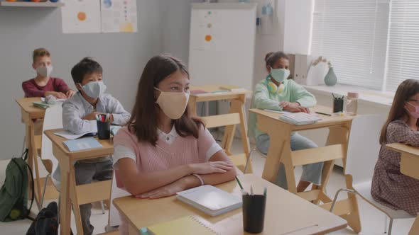 Kids in Face Masks Raising Hands in Class