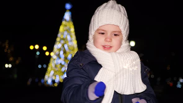 A Beautiful Christmas Child Plays with a Sparkler in Front of a Christmas Tree