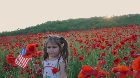 American baby girl with the US flag. Independence Day. Poppies field at sunset