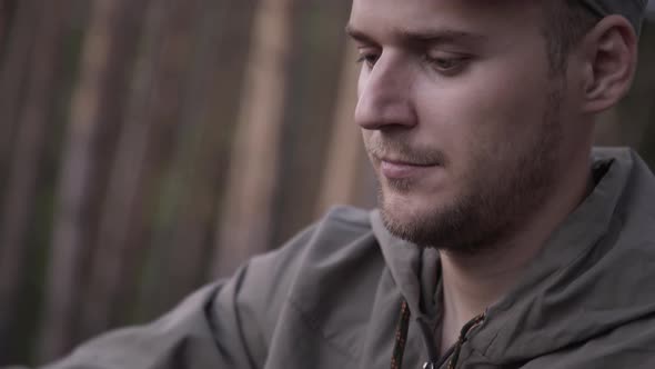 Portrait of Male Tourist Is Planing Wooden Peg with Knife in Summer Forest. Cooking Dinner on Wild