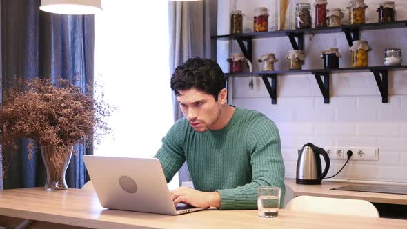 Amazed Happy Young Man Working on Laptop in Kitchen