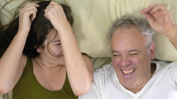 Happy funny young family couple laughing on bed mattress, active carefree husband and wife fun 4K