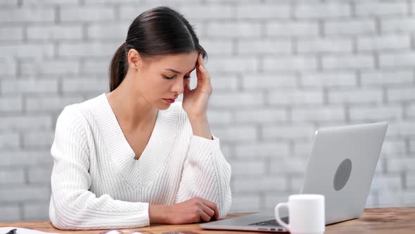 Tired Woman Massaging Temples Sitting in Front of Laptop