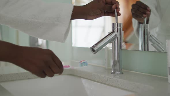 Hands of african american attractive woman applying toothpaste on the brush in bathroom