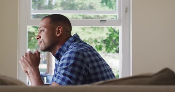 Side view of thoughtful biracial man sitting and looking outside window