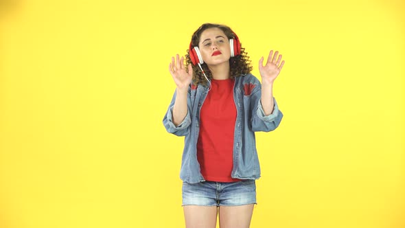Lovely Girl Dancing in Big Red Headphones on Yellow Background at Studio