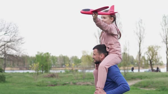 Happy family, dad, little daughter play together with a toy plane in the park.