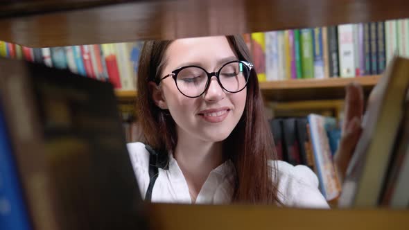 A University Student is Looking for a Book on Bookshelves in the Library