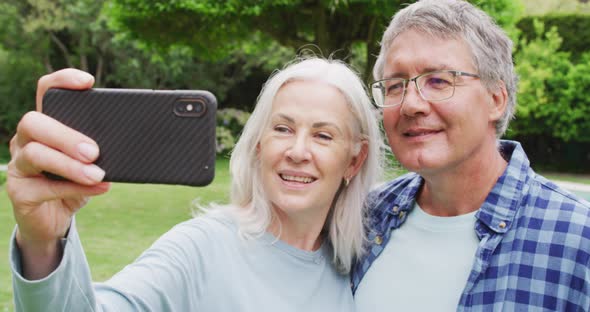 Animation of caucasian senior couple embracing in garden, taking selfie