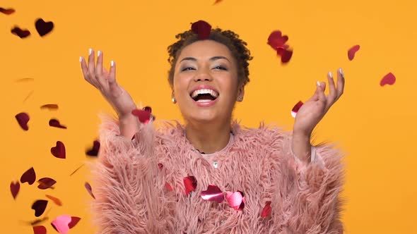 Joyful American Woman Standing Under Falling Heart-Shaped Confetti, Valentine